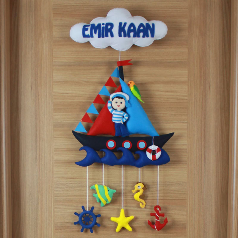 Yakın çekim: Keçe yelkenli tekne, denizci figürü ve Emir Kaan yazısı